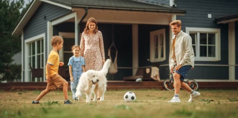 A family with a dog plays with a soccer ball outside.