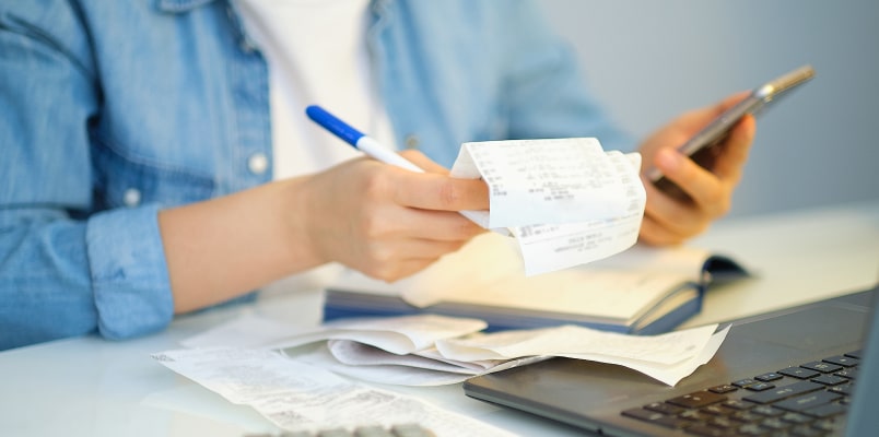 A close-up of a person reviewing receipts and using a phone while organizing finances to avoid a higher tax bracket.