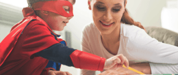 Boy dressed in superhero costume learning with smiling woman
