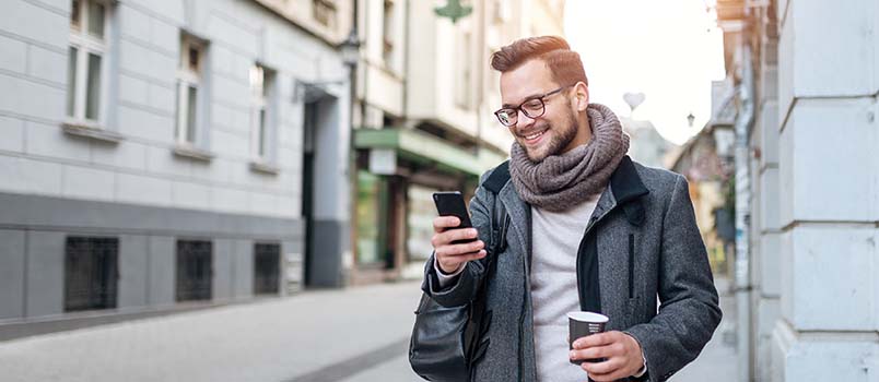A man walking on the street while holding a cup of coffee and mobile in his hands