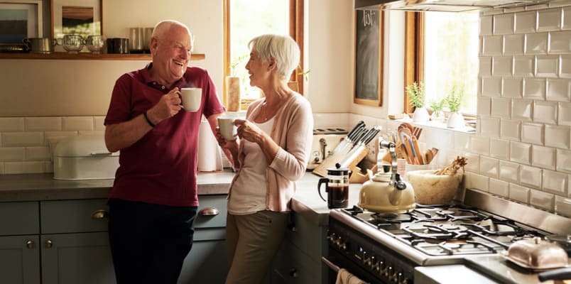 A smiling couple standing in a kitchen & drinking coffee together