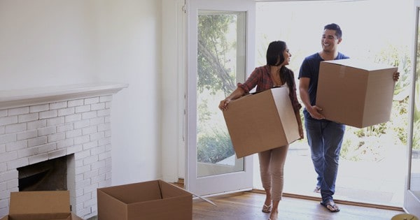A couple holding boxes in their hands while entering their new home.