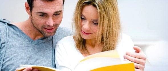 Young couple reading together a magazine in their living room at home.