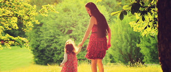 Back view of a mother and a small daughter walking together holding hands in the park