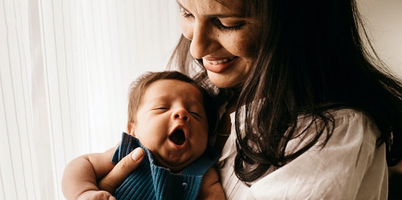 A smiling mother holds a yawning infant.