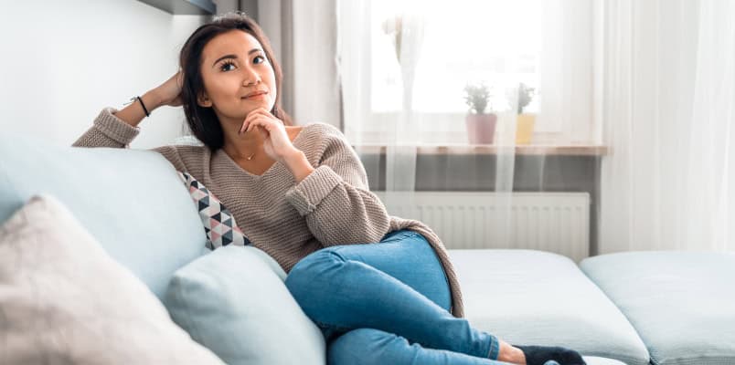 A young woman lounging on a couch and wondering whether she needs to file taxes this year