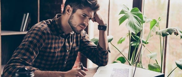 Man thinking in front of laptop and holding a pen