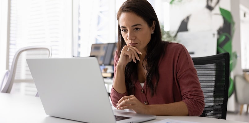 Business owner looking concerned while working on a laptop in a bright office.