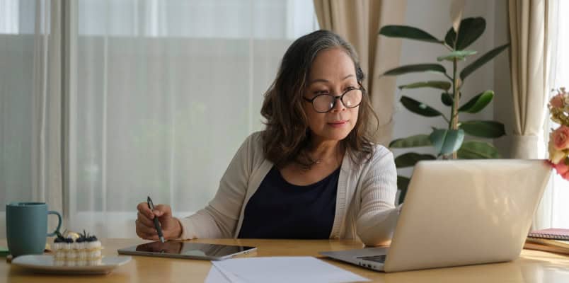 An older woman sitting in front of a laptop researching how to report her long-term care benefits on Form 1099-LTC