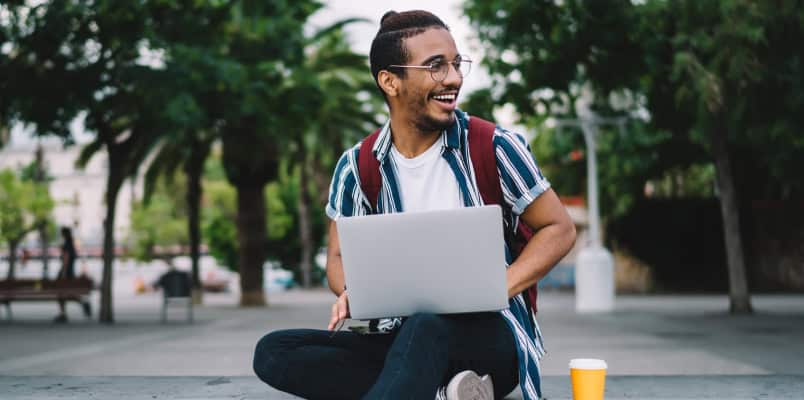 A smiling man sitting outside with his laptop as he reads about Form 1099-MISC