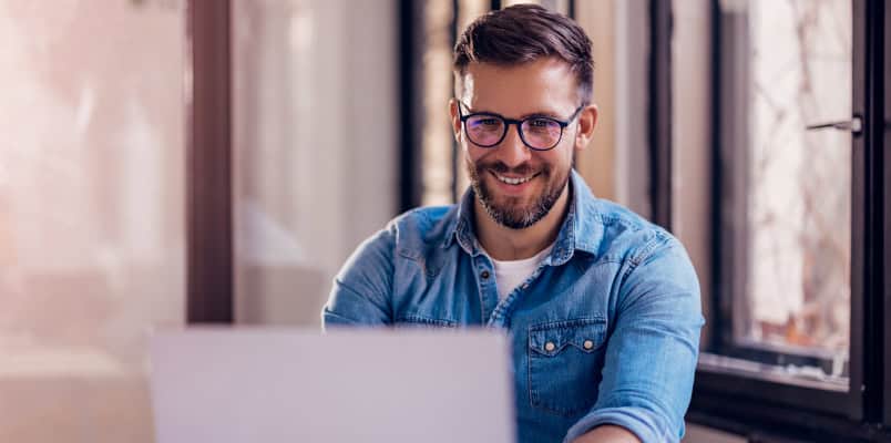 A man with glasses smiling as he e-files Form 1040 on his laptop