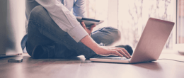 A man using a laptop on a floor along with a tablet.