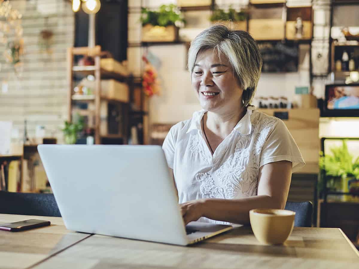 Smiling gray-haired middle aged businesswoman using laptop at living room