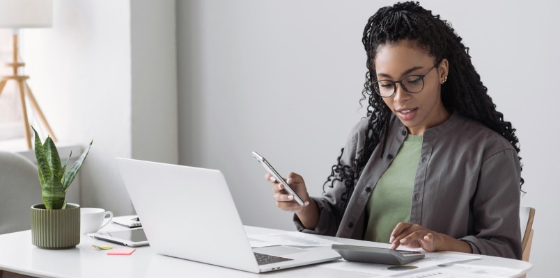 Woman using a calculator and laptop to figure out how to calculate and make estimated tax payments.