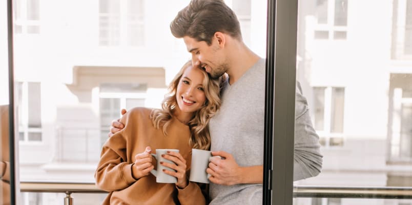 A woman and a man lean into each other while smiling and holding coffee mugs.