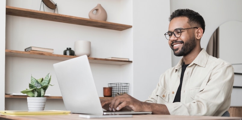A young adult man sits at a desk in a home office and uses a laptop to file taxes