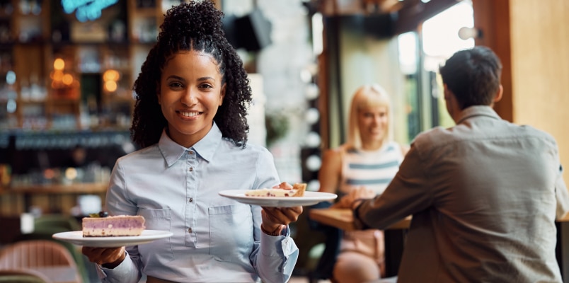 Smiling waitress carrying plates of food in a restaurant while learning about the new no tax on tips rule.