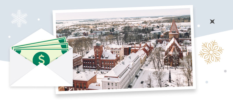 Beautiful city in winter with snow covered houses, churches and streets along with an image representation of a cash inside an envelope