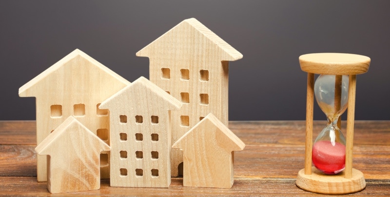 Five wooden house figurines next to an hourglass, representing the Augusta Rule for short-term rentals