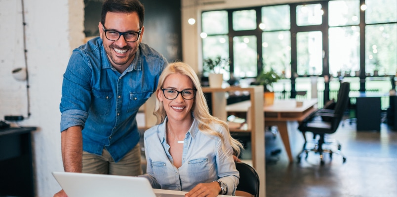Two smiling small business owners working together on a laptop in a modern office while reviewing the business tax return deadline with extension.