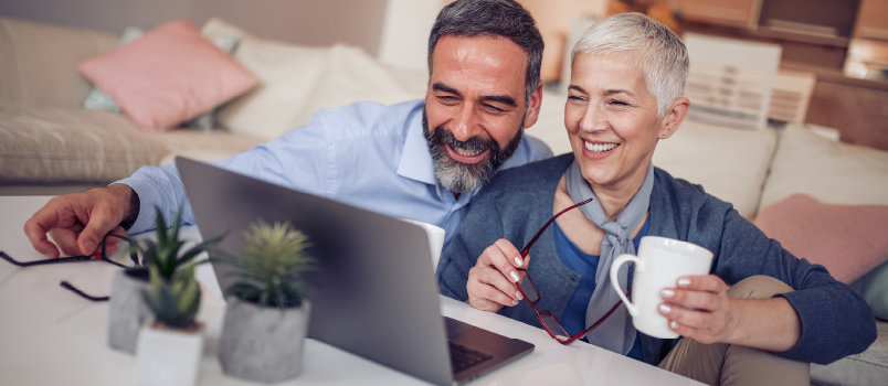 A smiling man and a woman holding a coffee cup in her hand while looking at her laptop