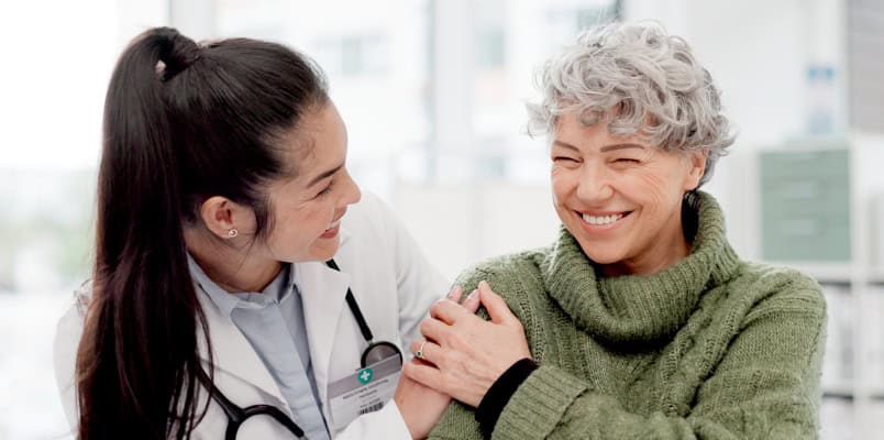 A doctor and her older patient smiling as they discuss health insurance