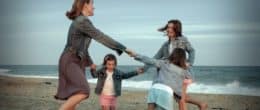 Mother and daughters holding hands playing on the seashore.