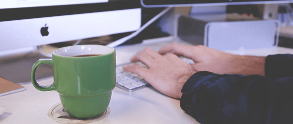 Hands on a keyboard with a coffee mug near