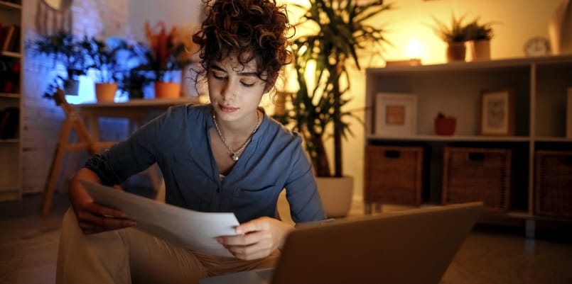 A woman in blue reviews her taxes in front of indoor palm trees backlit by a lovely yellow light