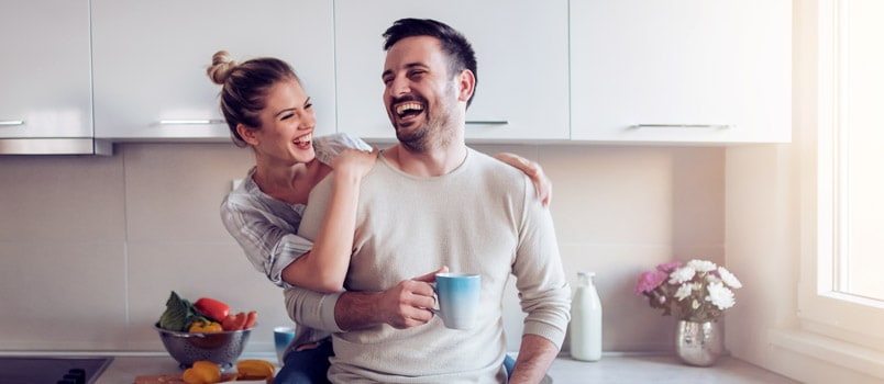 Happy couple in kitchen and man holding mug