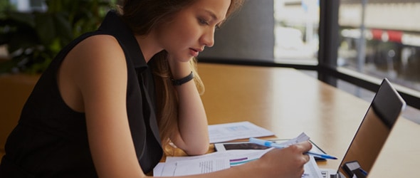 A woman sitting on a table in front of a laptop and wondering if she should file a tax extension