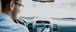 A man sitting in his car while using TaxAct's mileage reimbursement calculator on his smartphone