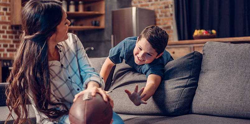 Little boy and his mom playing with a rugby ball on a couch