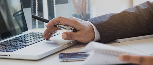 A man's hand pressing laptop key with a pen