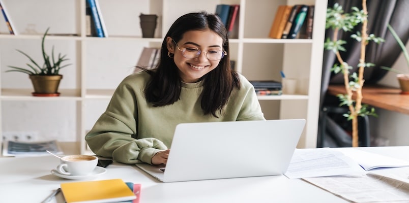 College student sits at desk in library, e-filing her taxes at a desk using her laptop