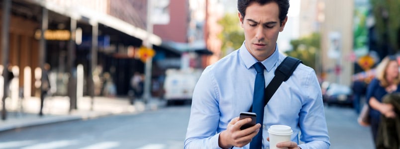 Man walking on street checking phone with one hand and holding coffee in another hand